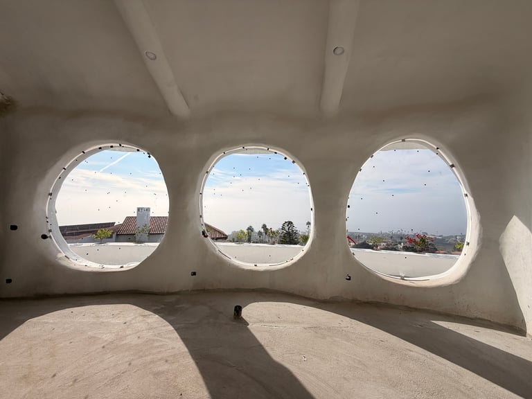 Vista interior a través de tres ventanas circulares de ojo de buey mostrando paisaje y cielo afuera de estructura de concreto