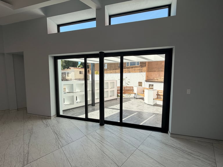 Cuarto moderno vacío con puertas de vidrio de marco negro hacia patio, piso de madera clara y ventanas clerestory