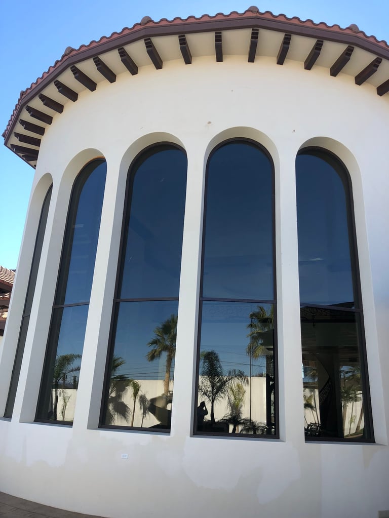 Fachada de edificio blanco curvo con cuatro ventanas arqueadas altas y borde decorativo de techo de tejas contra cielo azul