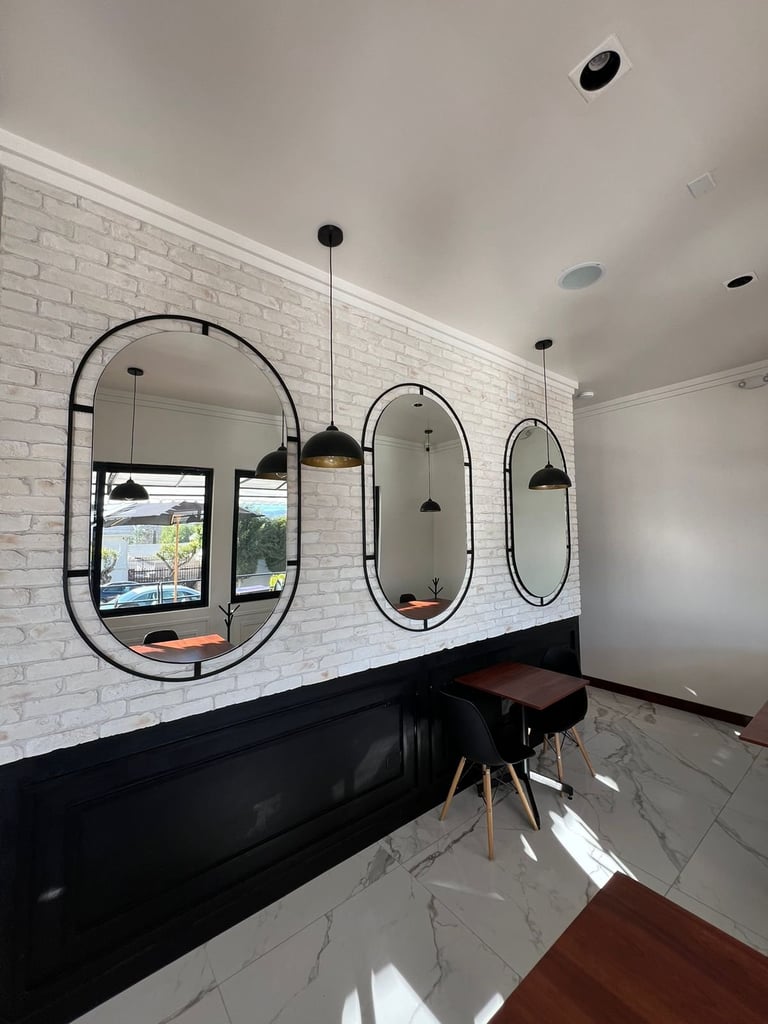 Baño moderno con tres espejos ovalados de marco negro, tocador negro, lámparas colgantes, pared de ladrillo blanco y piso de mármol