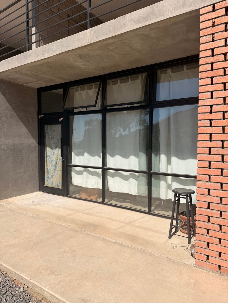 Fachada de edificio moderno con grandes puertas y ventanas de marco negro en patio de concreto junto a pared de ladrillo rojo