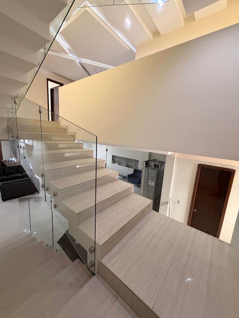 Interior moderno con escalera de madera clara, barandal de vidrio, paredes crema, tragaluces y decoración minimalista en espacio brillante