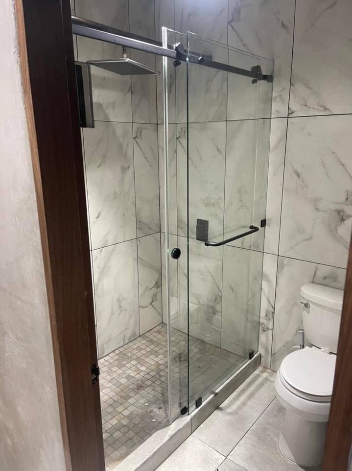Ducha de vidrio moderna con paredes de azulejo de mármol y marco cromado, adyacente a inodoro blanco en baño contemporáneo