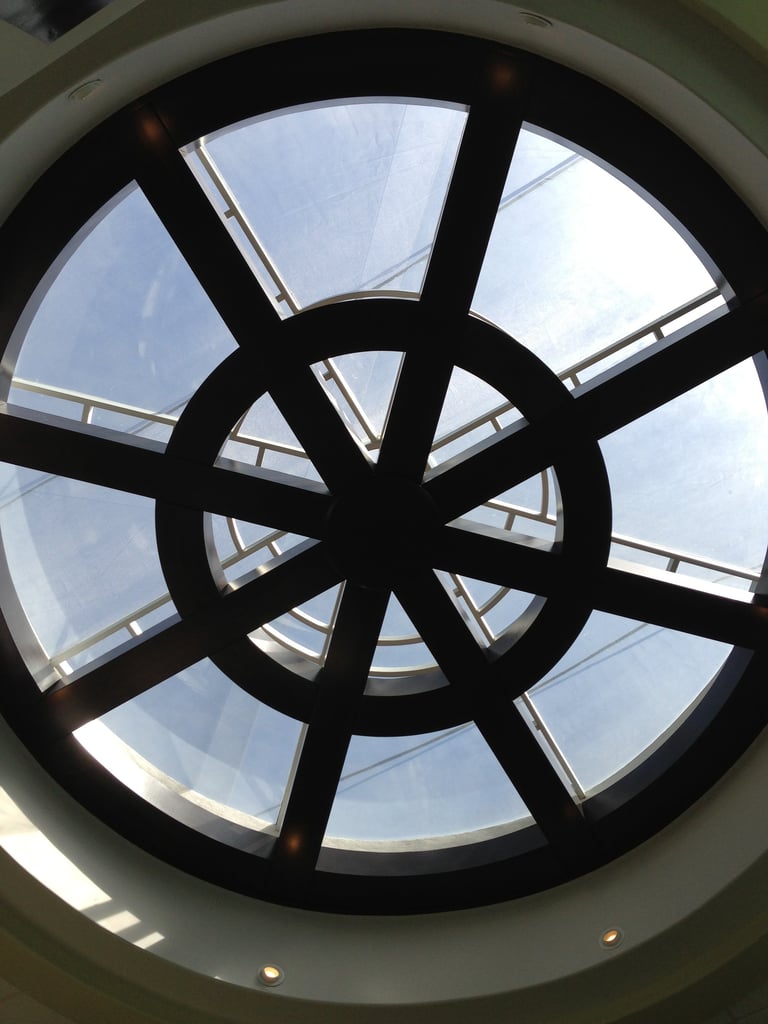 Ventana de tragaluz circular con divisores negros como rayos y paneles de vidrio mostrando vista del cielo azul desde abajo