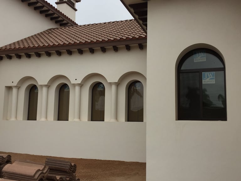 Edificio de estuco blanco con ventanas arqueadas y techo de madera oscura con tejas de terracota