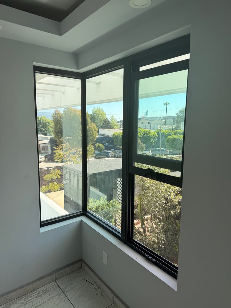 Ventana de esquina moderna con marcos negros sobresaliendo vecindario residencial y paisaje suburbano desde habitación con paredes grises