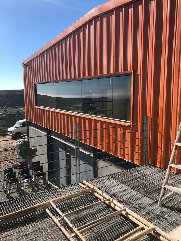 Edificio moderno de metal corrugado rojo con ventana horizontal grande y escalera de cubierta metálica, en paisaje rural