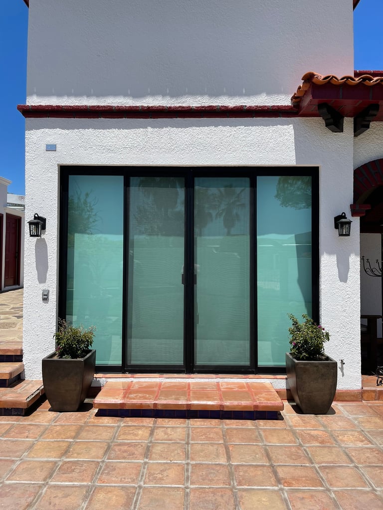 Exterior de edificio blanco moderno con puertas corredizas de vidrio de marco negro, patio de tejas de terracota y plantas en macetas