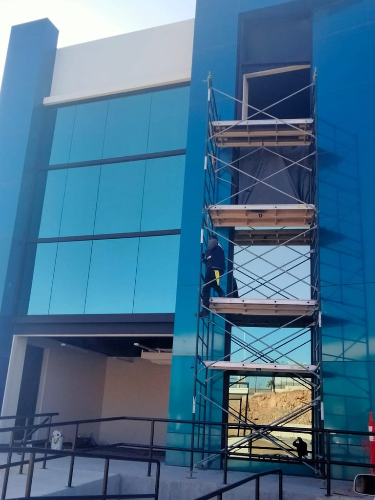 Edificio azul moderno en construcción con andamiaje metálico en el lado derecho y ventanas de vidrio en la fachada izquierda