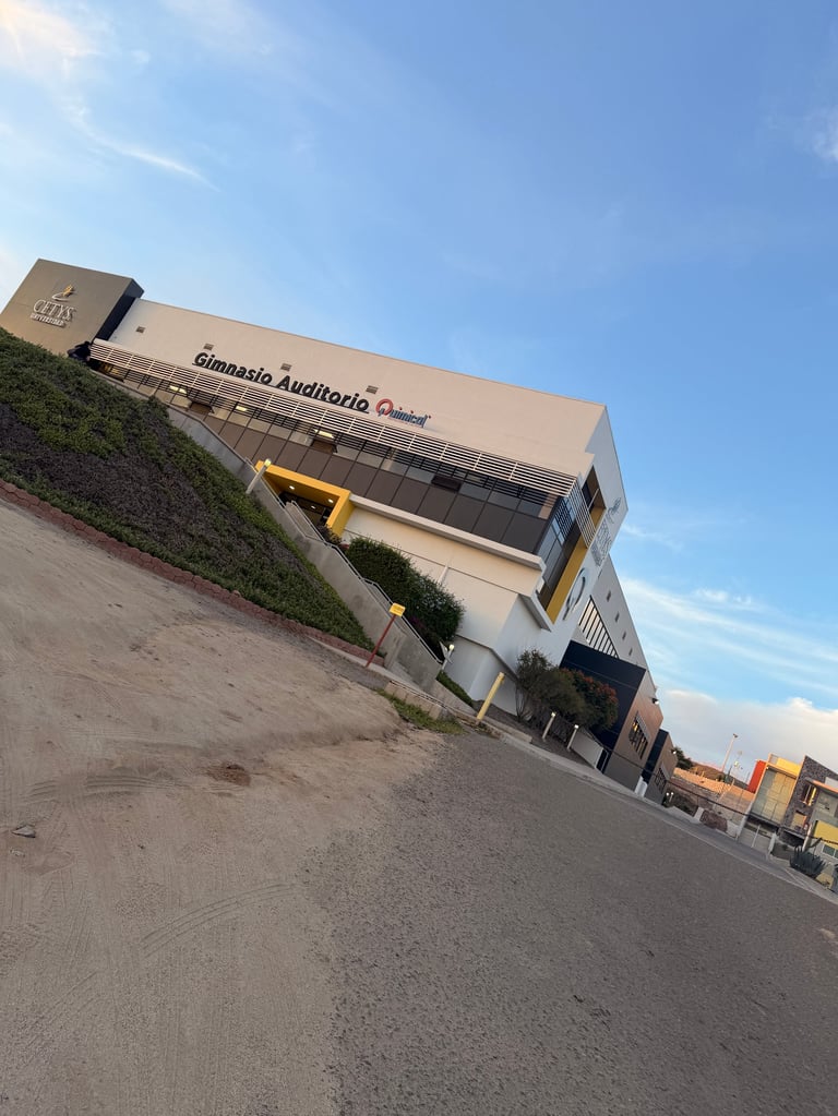 Gimnasio moderno con fachada beige y elementos estructurales amarillos en terreno inclinado